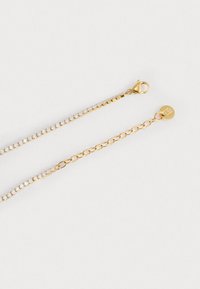 Braccialetto in oro con una fila di cristalli trasparenti, dotato di chiusura a gancio e dettaglio a forma di cerchio. Texture liscia e finitura lucida.