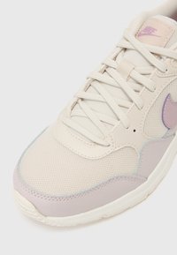 Beige Sneaker mit lila Akzenten, aus Mesh- und Synthetikmaterialien, runder Zehenform, dicker Sohle und hellen Schnürsenkeln.