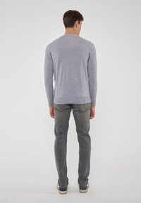 Maglione azzurro chiaro realizzato in maglia morbida, con maniche lunghe e scollatura rotonda, abbinato a jeans grigi aderenti e scarpe casual.