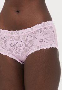 Pink lace boyshorts featuring floral patterns, scalloped edges, and a semi-sheer texture. Soft material with elastic waistband.