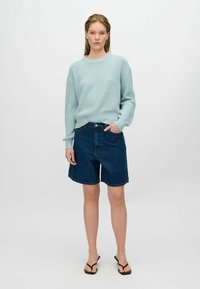 Light blue ribbed knit sweater with dropped shoulders, paired with dark blue denim shorts, and black flip-flops. Simple design, casual look.