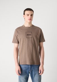 Brun, kortermet t-skjorte med rund hals, med en svart rektangulær "BOSS" logo i midten. Laget av et mykt, teksturert stoff.