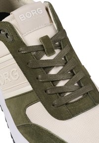 Schoen met een beige mesh bovenwerk en groene suède accenten, platte veters en een gestructureerde rubberen zool. "BORG STOCKHOLM" logo op de tong.