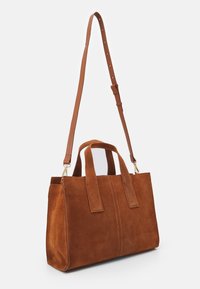 Sac à main en daim marron avec une forme structurée, deux anses supérieures et une bandoulière amovible. Présente des coutures visibles et une texture lisse.