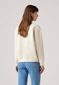 Felpa color crema con vestibilità comoda, polsini e orlo a costine, abbinata a jeans azzurri chiari texturizzati. Tessuto simile alla lana, design minimalista.