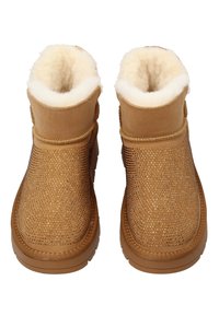 Beżowe botki za kostkę z teksturowaną, błyszczącą cholewką i miękką, białą podszewką ze sztucznego futra. Zaokrąglony nosek, przeszycia dekoracyjne oraz gumowa podeszwa.