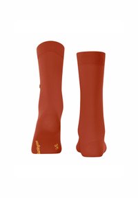 Une paire de chaussettes rouges présentées à la verticale, montrant des bords côtelés et une texture lisse, avec un petit logo sur le côté près de la cheville.