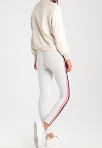 Light beige bomber jacket with elastic waistband paired with light gray leggings featuring side stripes in pink and black, complemented by white sneakers.