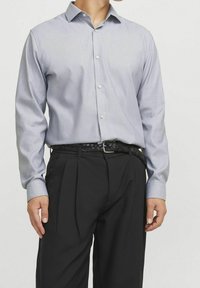 Camicia azzurra a maniche lunghe con una sottile texture, bottoni frontali e colletto a punta, indossata con pantaloni neri su misura e una cintura intrecciata nera.