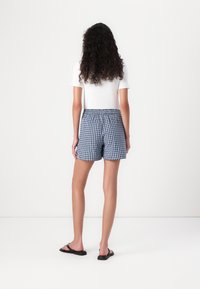 Shorts en vichy bleu et blanc avec une taille élastique, portés avec un t-shirt blanc ajusté, montrés de dos sur fond uni.