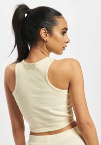 Beige ribbet crop topp med rund halslinning og brede armåpninger, som viser teksturert stoff og slank passform design.