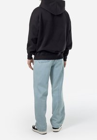 Svart munkjacka med huva och avslappnad passform, kombinerad med ljusblå jeansbyxor. Outfitten kompletteras med svarta sneakers.