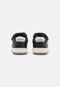 Ein Paar Schwarz-Weiß-Sneaker mit braunen Sohlen, von hinten betrachtet, mit "BOSS"-Logo auf den Fersenlaschen.