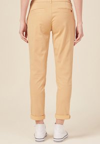Khaki chinos met een slim fit, opgerolde manchetten, twee achterzakken en een gladde textuur, gecombineerd met witte veterschoenen.