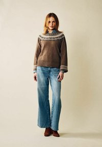 Ruskea neulottu neule, jossa on kuvioitu yläosa, yhdistetty vaaleansinisiin liehuviin farkkuihin. Asusteina ruskeat mokkanahkaiset nilkkurit ja sininen paita.