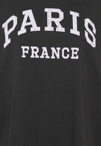 Camiseta de algodón negra con texto blanco en negrita "PARÍS FRANCIA" en una fuente desgastada, diseño curvado y mangas cortas.