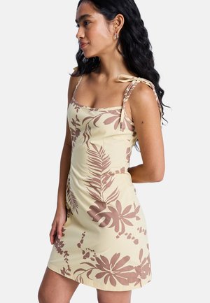 Robe jaune avec motifs floraux marron, dotée de fines bretelles et d'un détail noué sur les épaules. Coupe ajustée avec un ourlet court.