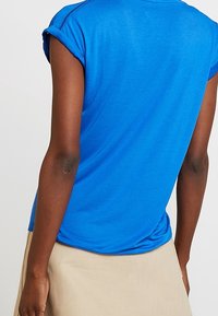 Camiseta de manga corta azul con mangas enrolladas, hecha de una tela suave, con un dobladillo redondeado y un detalle de costura mínima en los hombros.