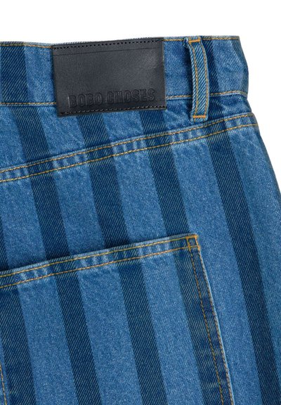 Blau gestreifter Denimstoff mit gelber Naht und einem schwarzen Lederpatch mit Prägung "BOBO CHOSES" oberhalb einer Gesäßtasche.