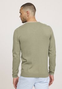 Pull en maille verte avec manches longues et poignets côtelés. Possède un col rond et une finition texturée à l'arrière.
