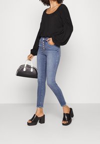 Svart långärmad Blus med samlingsdetalj, parat med högmidjade ljusblå skinny jeans, svarta klackskor med blocktopp och en svart handväska.