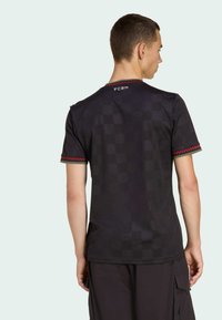 Man wearing black short-sleeve shirt with subtle checkerboard pattern and red checkered trim on sleeves and collar, facing away.