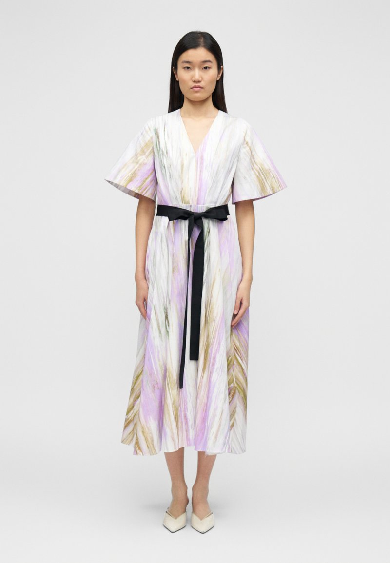 Obleka srednje dolžine iz belega blaga z vijolično in zlato abstraktno vzorcem. Ima široke rokave in črni pas v pasu. Čevlji s kvadratnimi konicami.