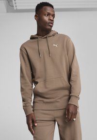 Sudadera con capucha marrón hecha de un material suave, con un bolsillo canguro y pequeño logo blanco de Puma en el pecho. Ajuste cómodo.