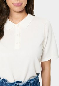 Kurzärmliges, kragenloses Polohemd aus weichem, weißem Rippstoff. Verfügt über eine Knopfleiste und einen lässigen Schnitt mit einfachen, klaren Linien.