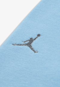 Material de culoare bleu deschis cu o textură netedă; prezintă un logo Jumpman brodat în negru, poziționat central.
