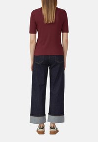 Bordeaux kleurig kortemouwen top met wijde donkerblauwe jeans met opgerolde hems en bruine plateauschoenen. Glad materiaal met een casual pasvorm.