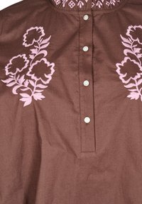 Camicia di cotone marrone con ricami floreali rosa sul davanti, una parte di bottoni e un dettaglio di scollo arricciato.