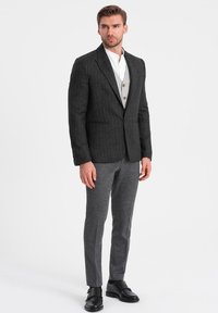 Blazer a righe grigio carbone con due tasche frontali, rever a scollo a V, texture morbida. Abbinato a pantaloni grigi e scarpe nere.