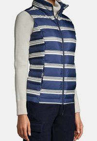 Marineblau gestreifte Steppweste mit weißen horizontalen Streifen, hohem Kragen, Frontreißverschluss und einer gepolsterten Textur; getragen über einem leichten Pullover.