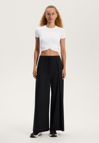 Biely krátky crop top s nariasením vpredu, skombinovaný s čiernymi širokými nohavicami s nastaviteľným pásom.