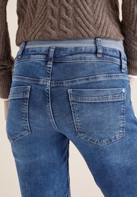 Modré džínové kalhoty středního praní s klasickým designem pěti kapes a mírně zúženými nohavicemi. Texturovaná látka s jemnými vybledlými detaily.