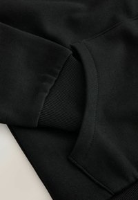 Černá mikina z materiálu s žebrovanými manžetami, která vykazuje hladkou texturu a rovnoměrné švy. Navržena v jednoduchém, moderním střihu.