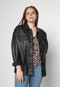 Casaco de couro preto com um design estruturado, botões de pressão e dois bolsos frontais, sobreposto a uma blusa com padrão de leopardo cor-de-rosa e jeans azuis.