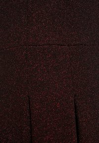 Jupe noire avec un subtil éclat, présentant une finition texturée. Elle comprend des détails de plis, offrant un design structuré et un intérêt visuel.