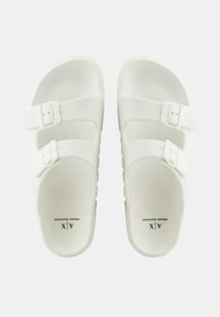 Sandalias deslizantes blancas con dos hebillas ajustables, suelas planas, plantilla texturizada y un ligero contorno para mayor comodidad.