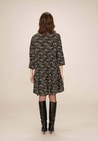 Robe florale noire à manches trois-quarts, coupe ample et ourlet froncé. Portée avec des bottes noires jusqu'aux genoux. Subtil motif texturé sur l'ensemble.