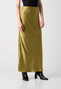 Satin olive green maxi skirt with a smooth texture, a simple silhouette, and a high waist, paired with glossy black heeled ankle boots.