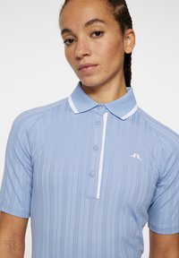 Polo shirt azzurro chiaro in trama a costine con colletto bianco, maniche corte e pattina con bottoni. Presenta un piccolo logo sul petto.