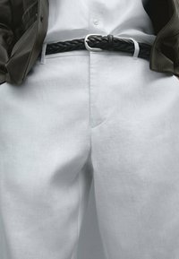 Weiße Leinenhosen mit einer lockeren Passform, kombiniert mit einem schwarzen geflochtenen Leder-Gürtel mit einer silbernen Schnalle, unter einer braunen Lederjacke.