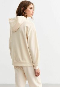 Krämfärgad hoodie med en mjuk textur, med dragsträngshuva, ribbade ärmar och en avslappnad passform, i kombination med matchande sweatpants.
