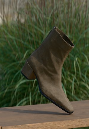 Bottine en daim marron avec un petit talon épais posée sur une surface en bois, arrière-plan de gazon vert flou.