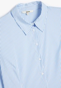 Camisa de botón a rayas azul claro y blanca, con cuello, mangas largas y un solo bolsillo en el pecho. Hecha de una tela suave.