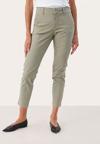 Pantalons slim vert clair avec poches latérales, légèrement extensibles et avec des poignets aux chevilles, associés à des ballerines noires à bout pointu.