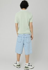 Polo shirt en maille vert clair, shorts en denim bleu clair, baskets noires et blanches avec des accents verts. Vu de dos.