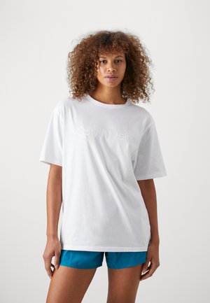 T-shirt bianco in cotone a maniche corte, con logo "Calvin Klein" in rilievo. Abbinato a pantaloni corti teal. Taglio semplice e rilassato.